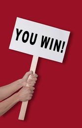 Image of Man holding sign with phrase You Win against dark red background, closeup