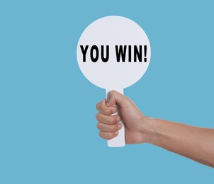 Image of Man holding sign with phrase You Win against light blue background, closeup