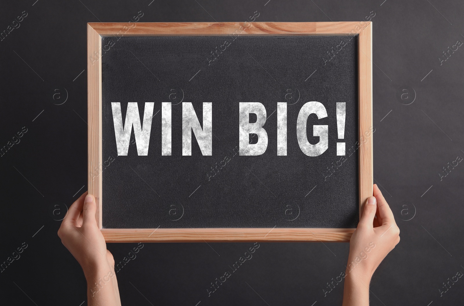 Image of Woman holding chalkboard with phrase Win Big against dark background, closeup