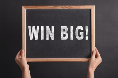Image of Woman holding chalkboard with phrase Win Big against dark background, closeup