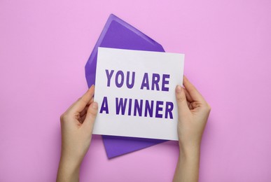 Image of Woman holding letter with phrase You Are A Winner on violet background, top view