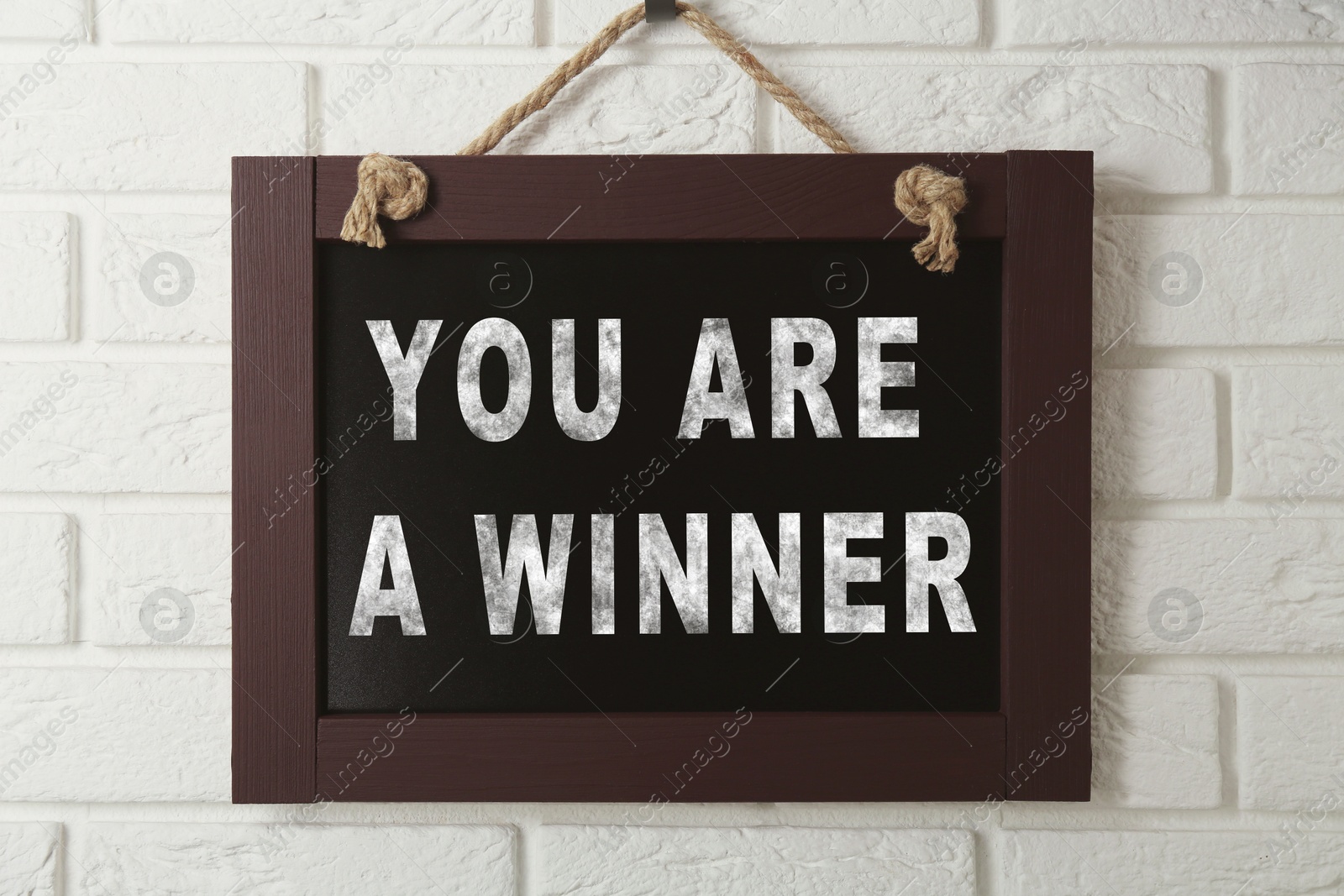 Image of Chalkboard with phrase You Are A Winner hanging on white brick wall