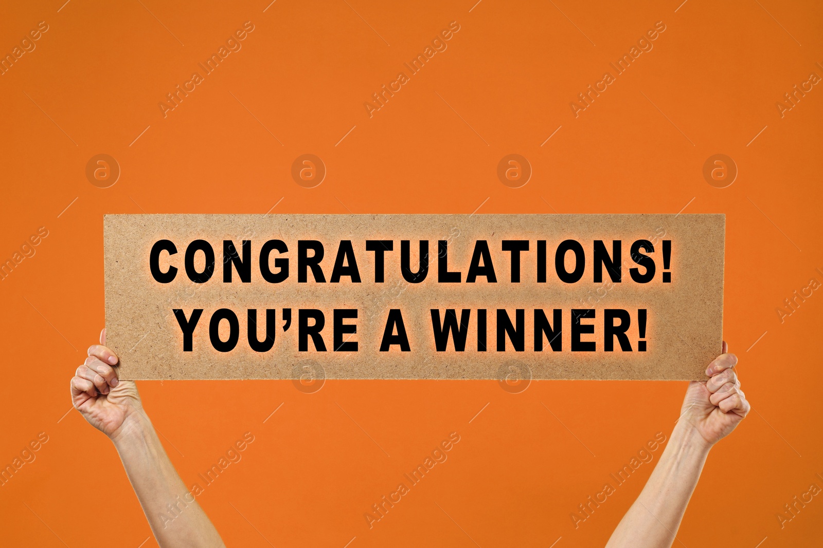 Image of Woman holding sign with phrase Congratulations! You're A Winner! against orange background, closeup