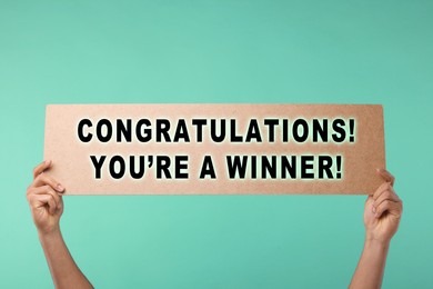 Image of Man holding sign with phrase Congratulations! You're A Winner! against turquoise background, closeup