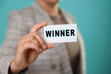 Image of Woman showing card with word Winner against light blue background, closeup