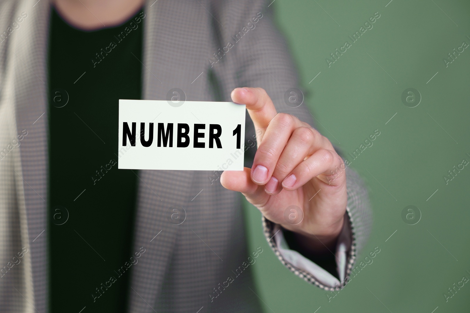 Image of Winner. Woman showing card with word Number 1 against greyish green background, closeup