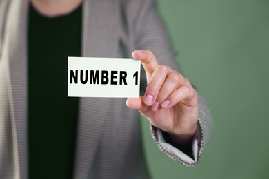 Image of Winner. Woman showing card with word Number 1 against greyish green background, closeup