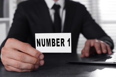 Image of Winner. Man showing card with word Number 1 at table, closeup