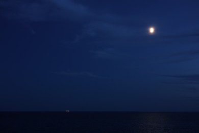 Photo of Moon glowing in night sky over beautiful sea with illuminated ship on horizon