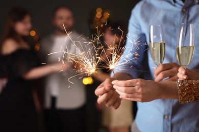 Photo of Friends celebrating New Year with sparklers and wine glasses indoors, closeup
