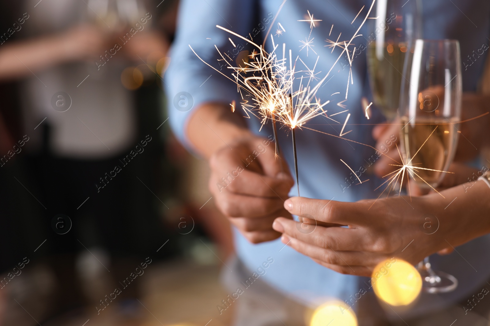 Photo of Friends celebrating New Year with sparklers and wine glasses indoors, closeup