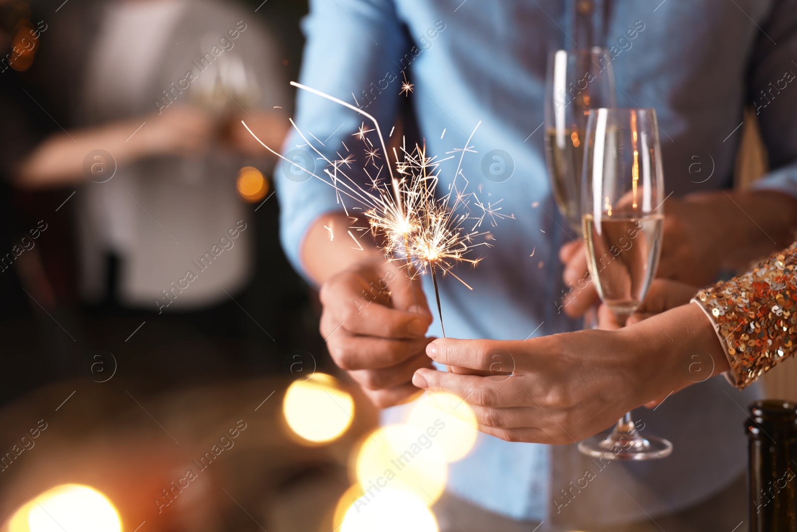 Photo of Friends celebrating New Year with sparklers and wine glasses indoors, closeup