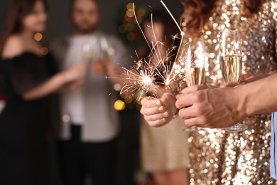 Photo of Friends celebrating New Year with sparklers and wine glasses indoors, closeup