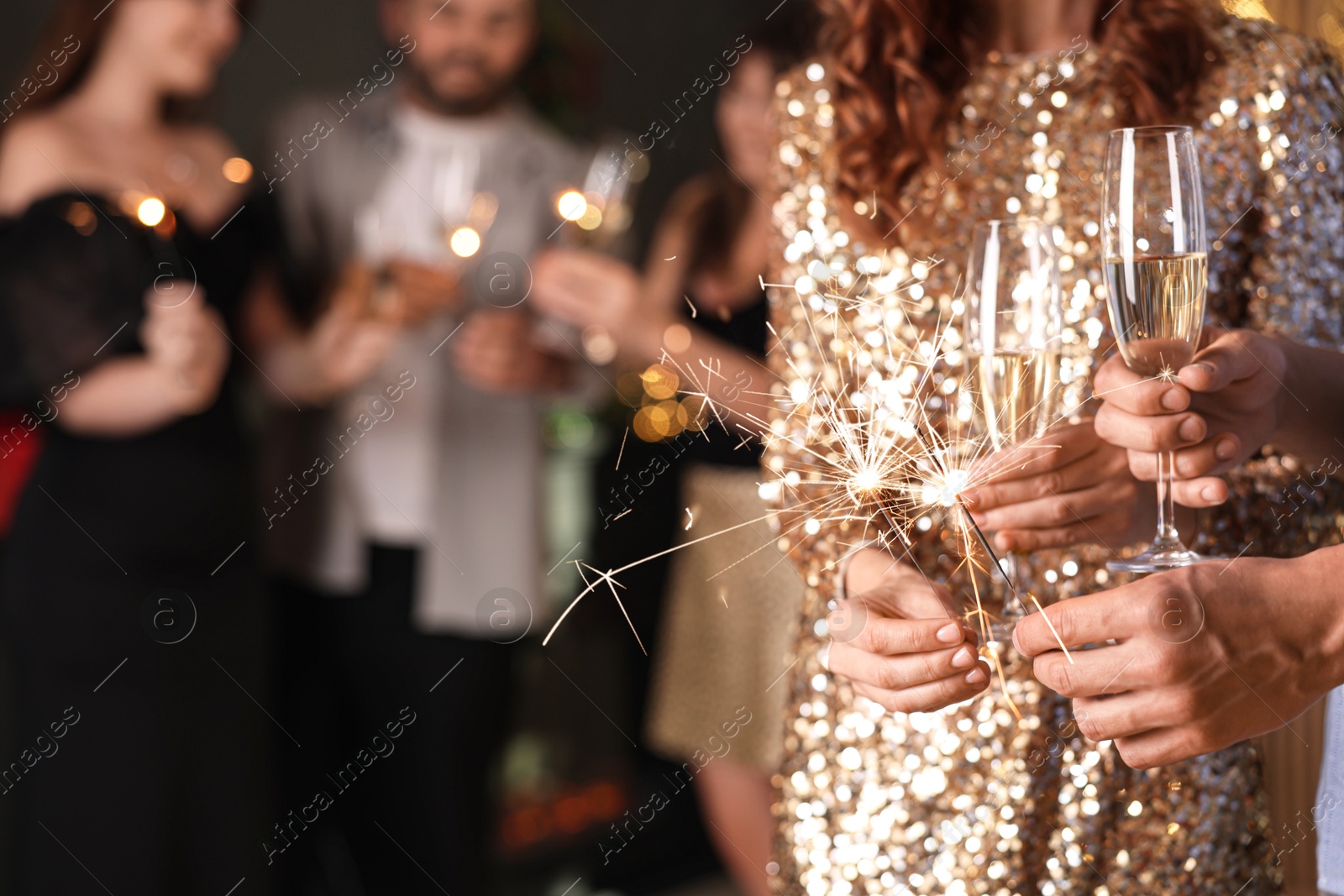 Photo of Friends celebrating New Year with sparklers and wine glasses indoors, closeup