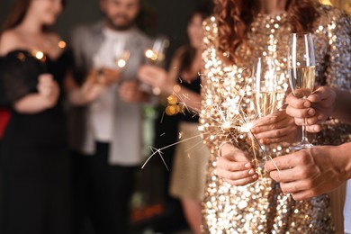 Photo of Friends celebrating New Year with sparklers and wine glasses indoors, closeup