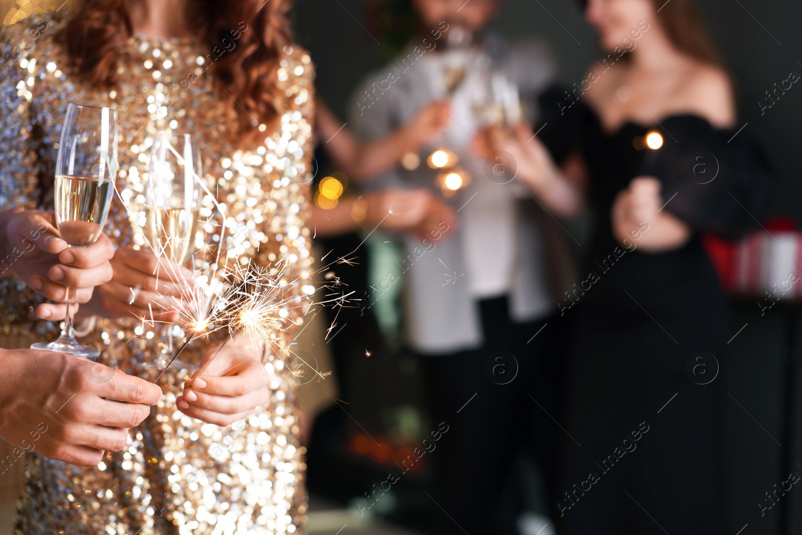 Photo of Friends celebrating New Year with sparklers and wine glasses indoors, closeup