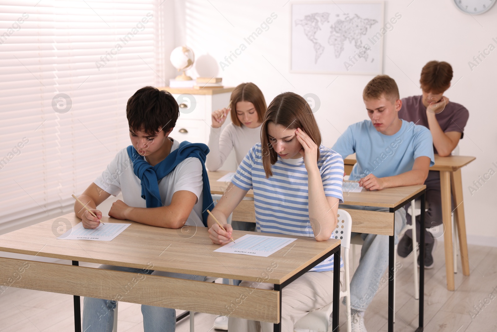 Photo of Students taking exam at wooden table indoors
