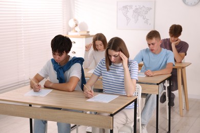 Photo of Students taking exam at wooden table indoors