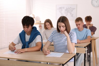 Photo of Students taking exam at wooden table indoors