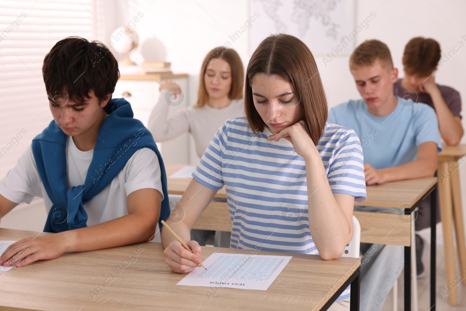 Photo of Students taking exam at wooden table indoors