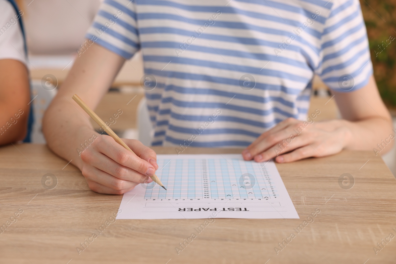 Photo of Student filling out answer sheet at wooden table indoors, closeup. Taking exam
