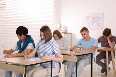 Photo of Students taking exam at wooden table indoors