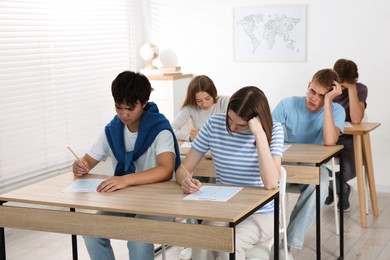 Photo of Students taking exam at wooden table indoors