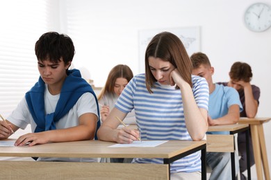 Photo of Students taking exam at wooden table indoors