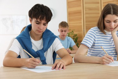 Photo of Students taking exam at wooden table indoors