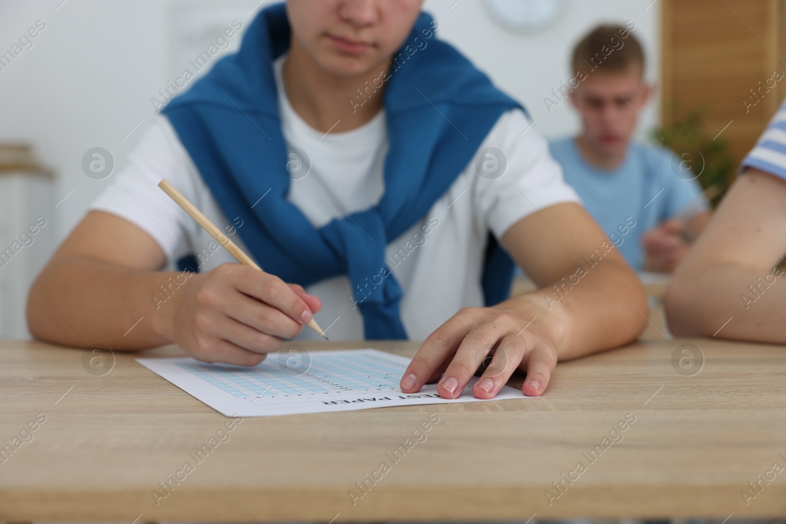 Photo of Students taking exam at wooden table indoors, selective focus