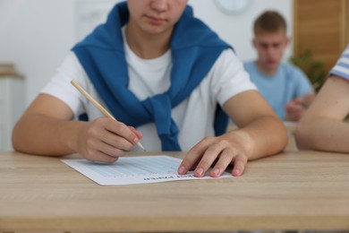 Photo of Students taking exam at wooden table indoors, selective focus