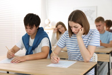 Photo of Students taking exam at wooden table indoors