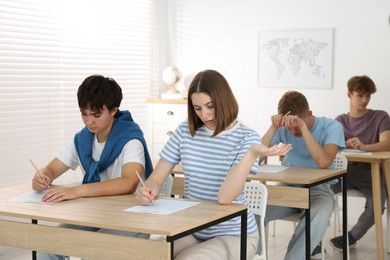Photo of Students taking exam at wooden table indoors