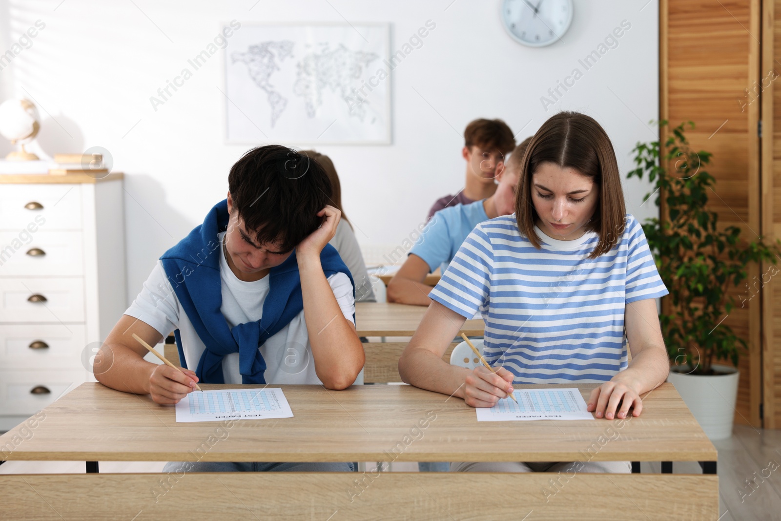 Photo of Students taking exam at wooden table indoors