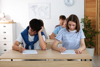 Photo of Students taking exam at wooden table indoors