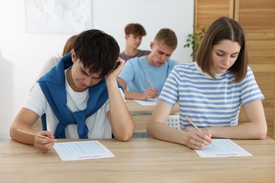 Photo of Students taking exam at wooden table indoors