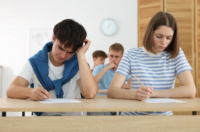 Photo of Students taking exam at wooden table indoors