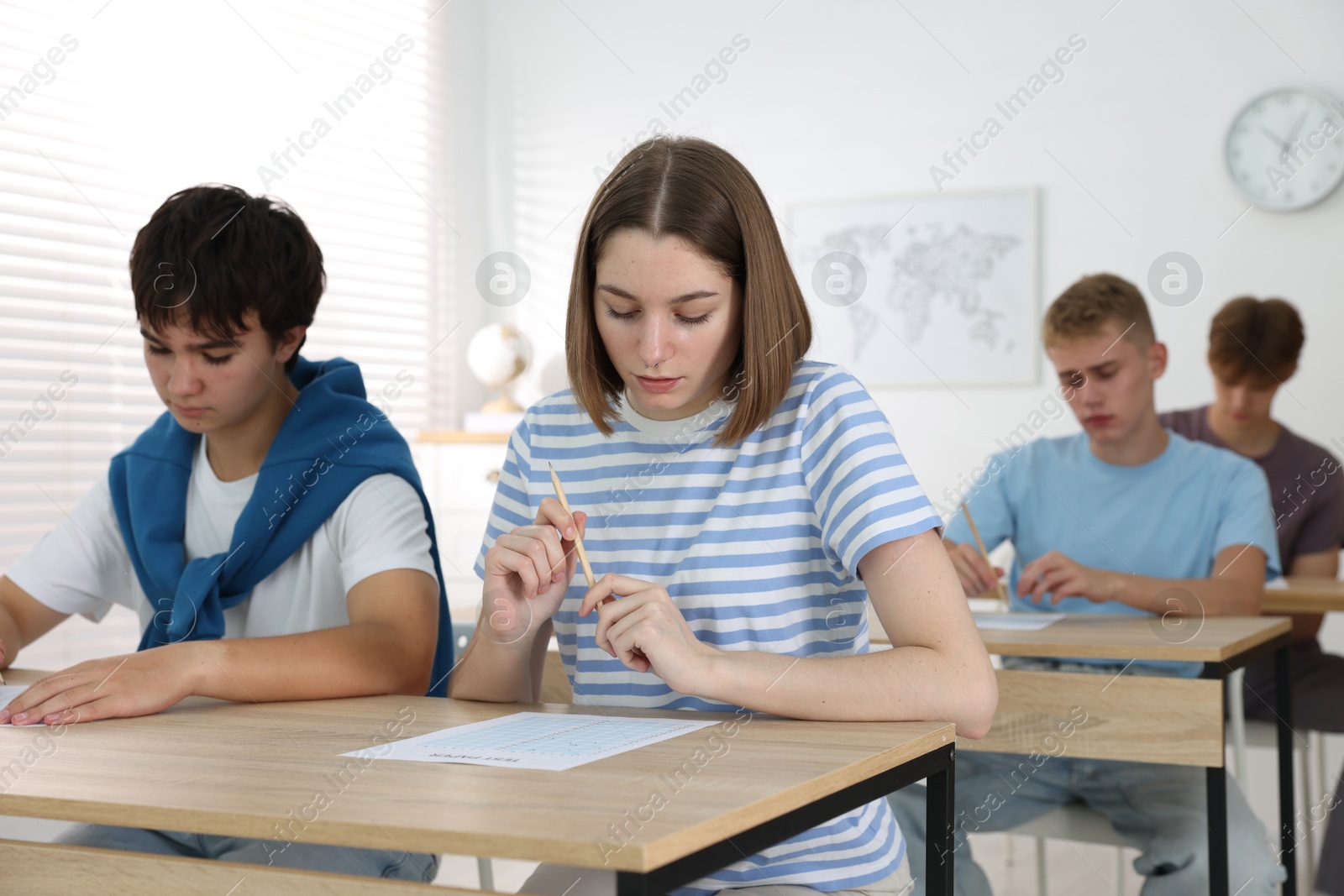 Photo of Students taking exam at wooden table indoors