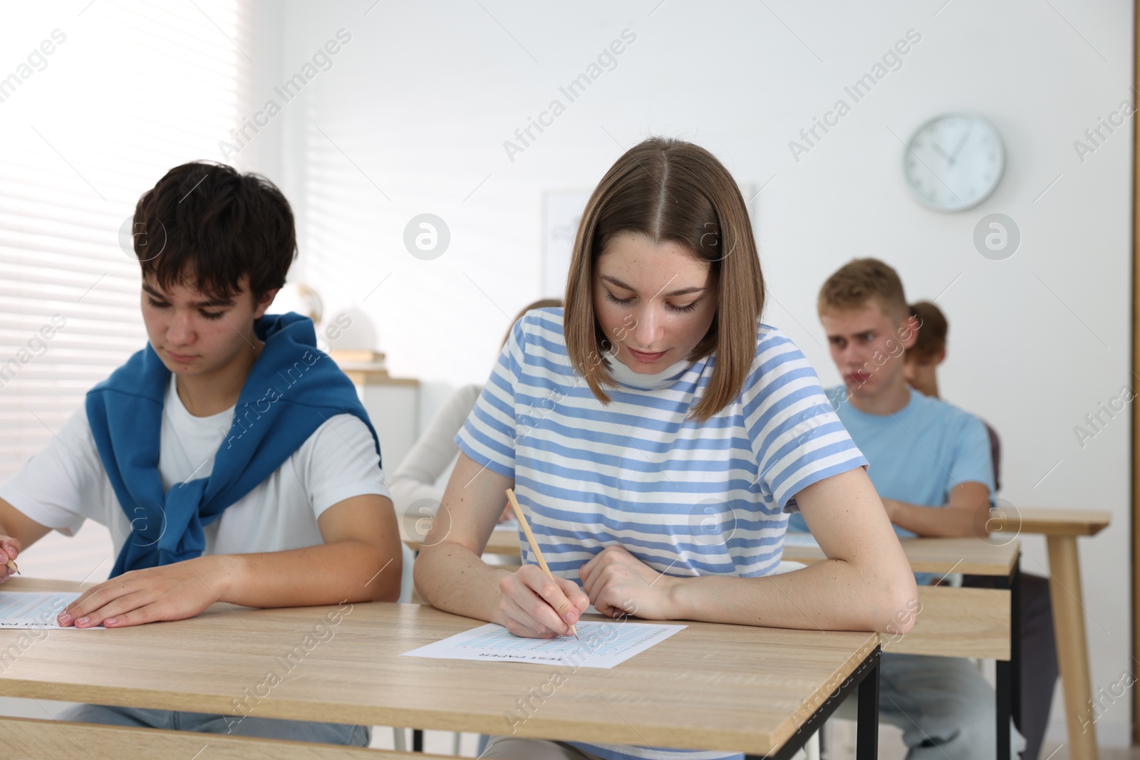 Photo of Students taking exam at wooden table indoors