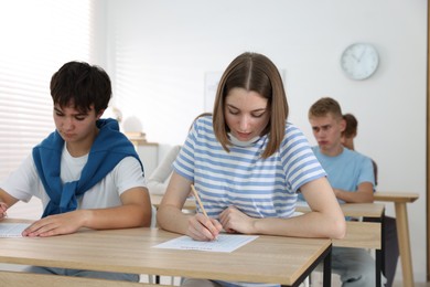 Photo of Students taking exam at wooden table indoors