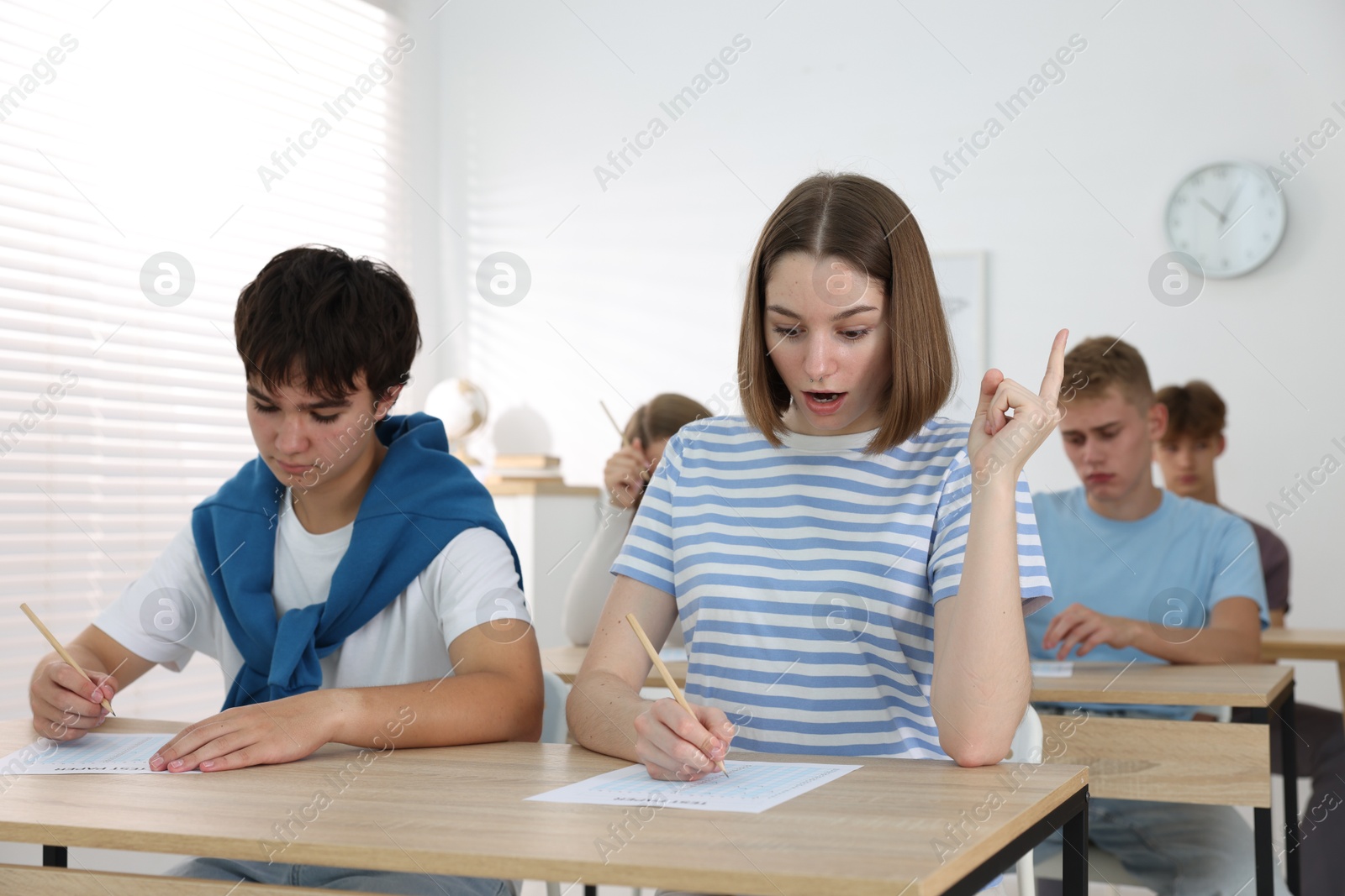 Photo of Students taking exam at wooden table indoors