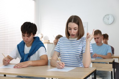Photo of Students taking exam at wooden table indoors