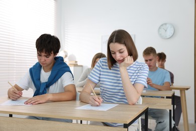 Photo of Students taking exam at wooden table indoors