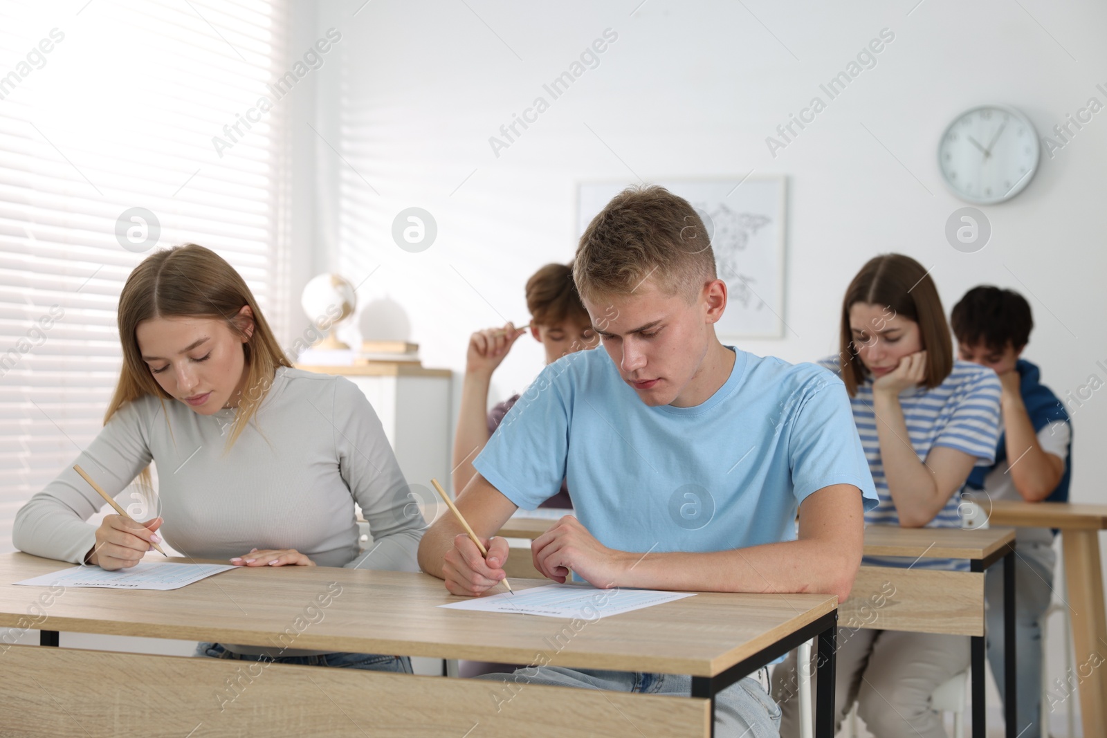 Photo of Students taking exam at wooden table indoors