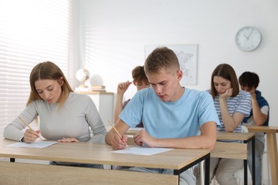 Photo of Students taking exam at wooden table indoors
