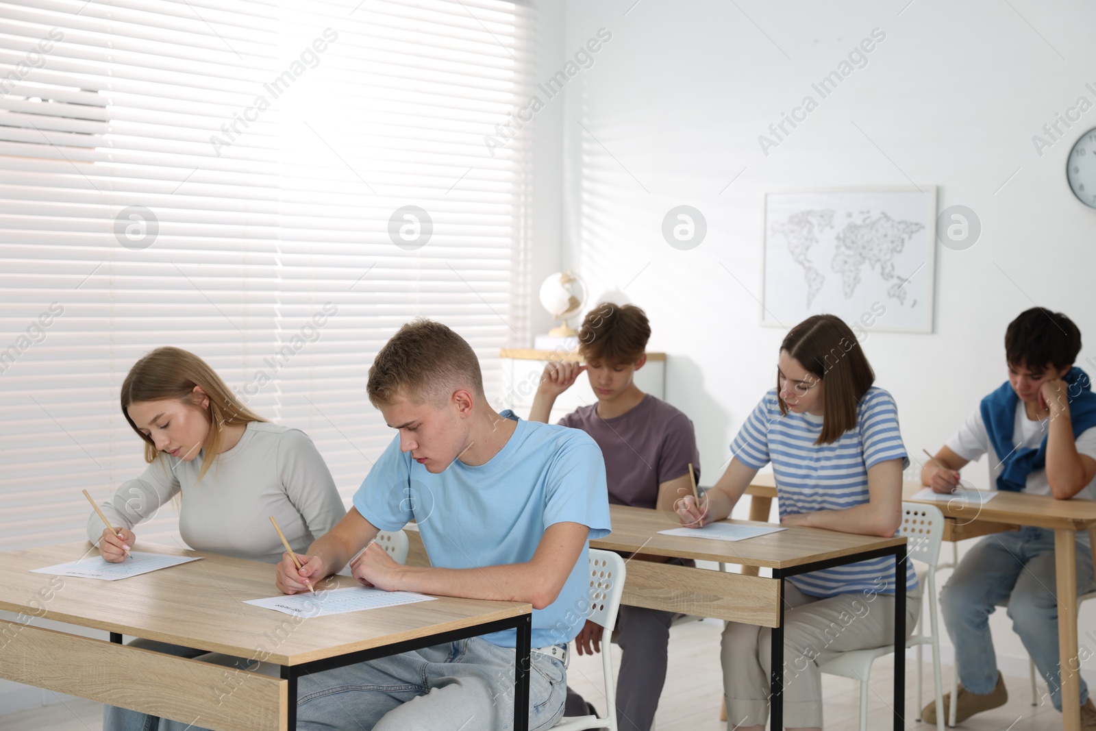 Photo of Students taking exam at wooden table indoors