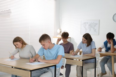 Photo of Students taking exam at wooden table indoors