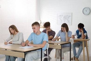 Photo of Students taking exam at wooden table indoors