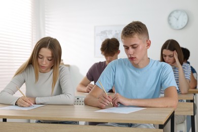 Photo of Students taking exam at wooden table indoors