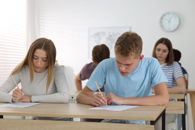Photo of Students taking exam at wooden table indoors